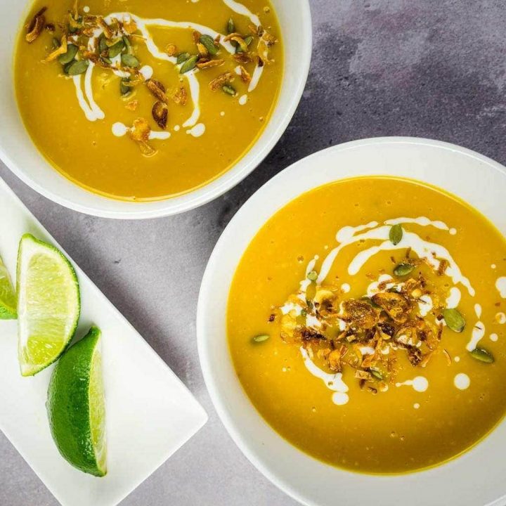 2 bowls of spicy Thai pumpkin soup with lime wedges
