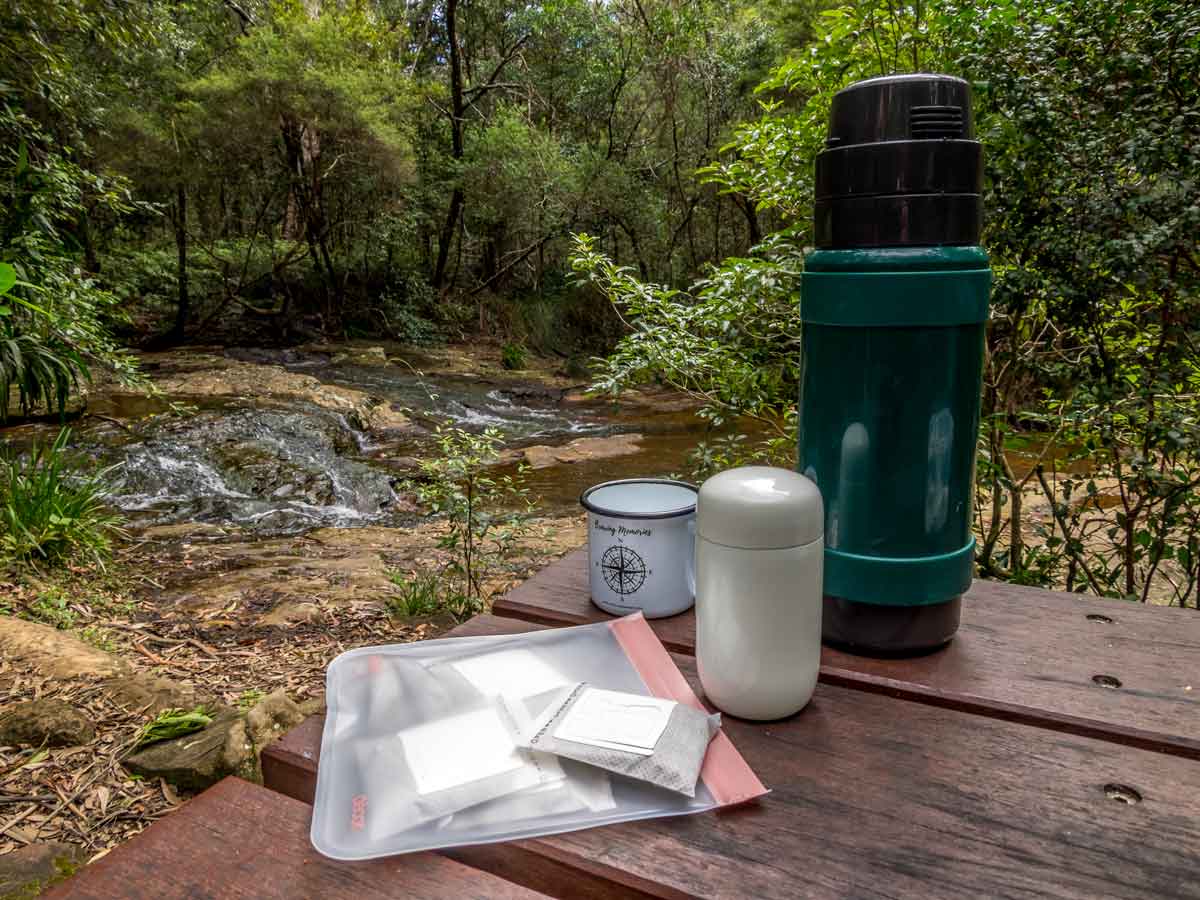 thermos and coffee gear on picnic table by stream