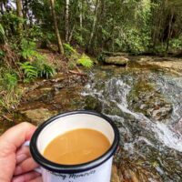 Coffee in enamel mug beside stream in rainforest