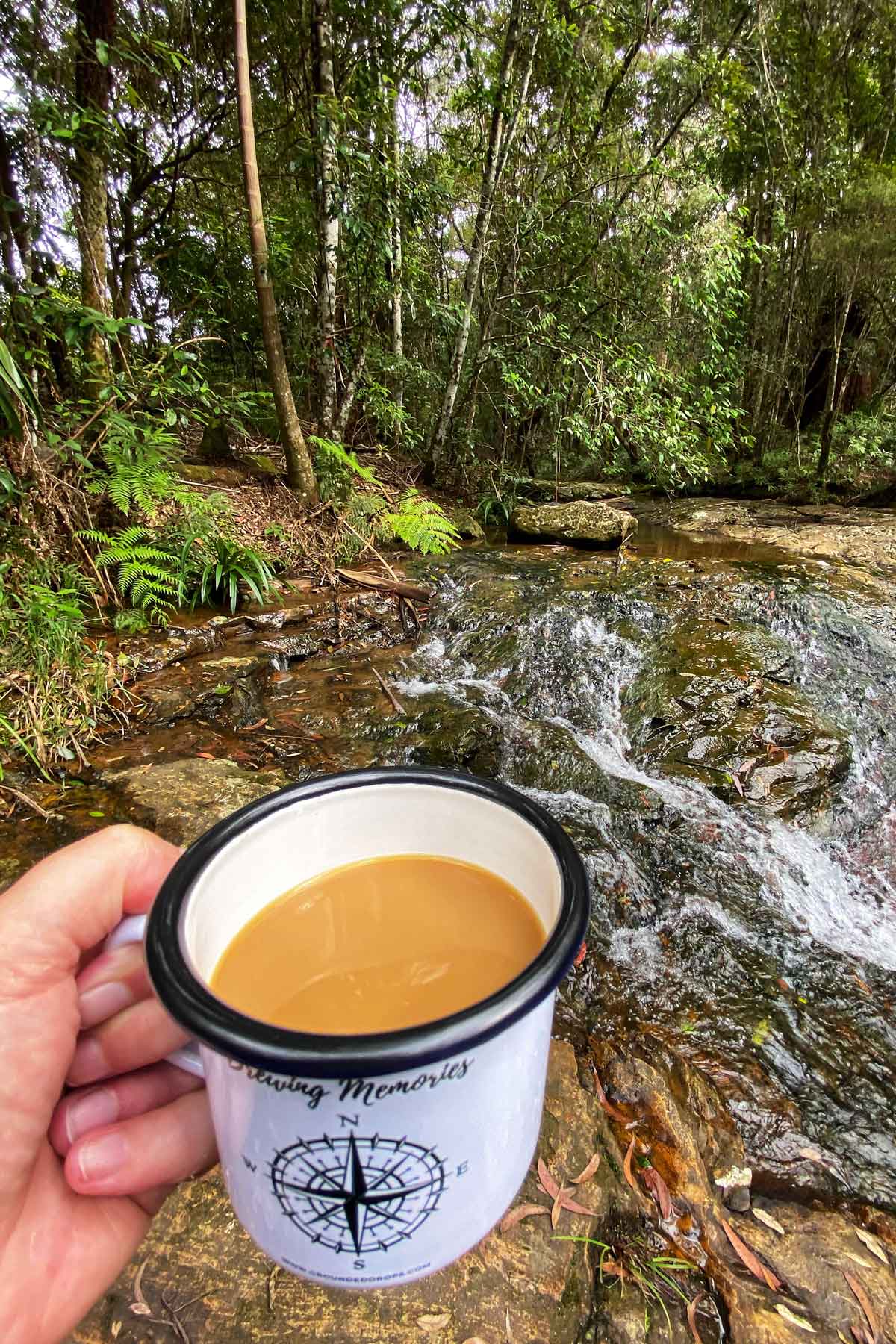 Coffee in enamel mug beside stream in rainforest