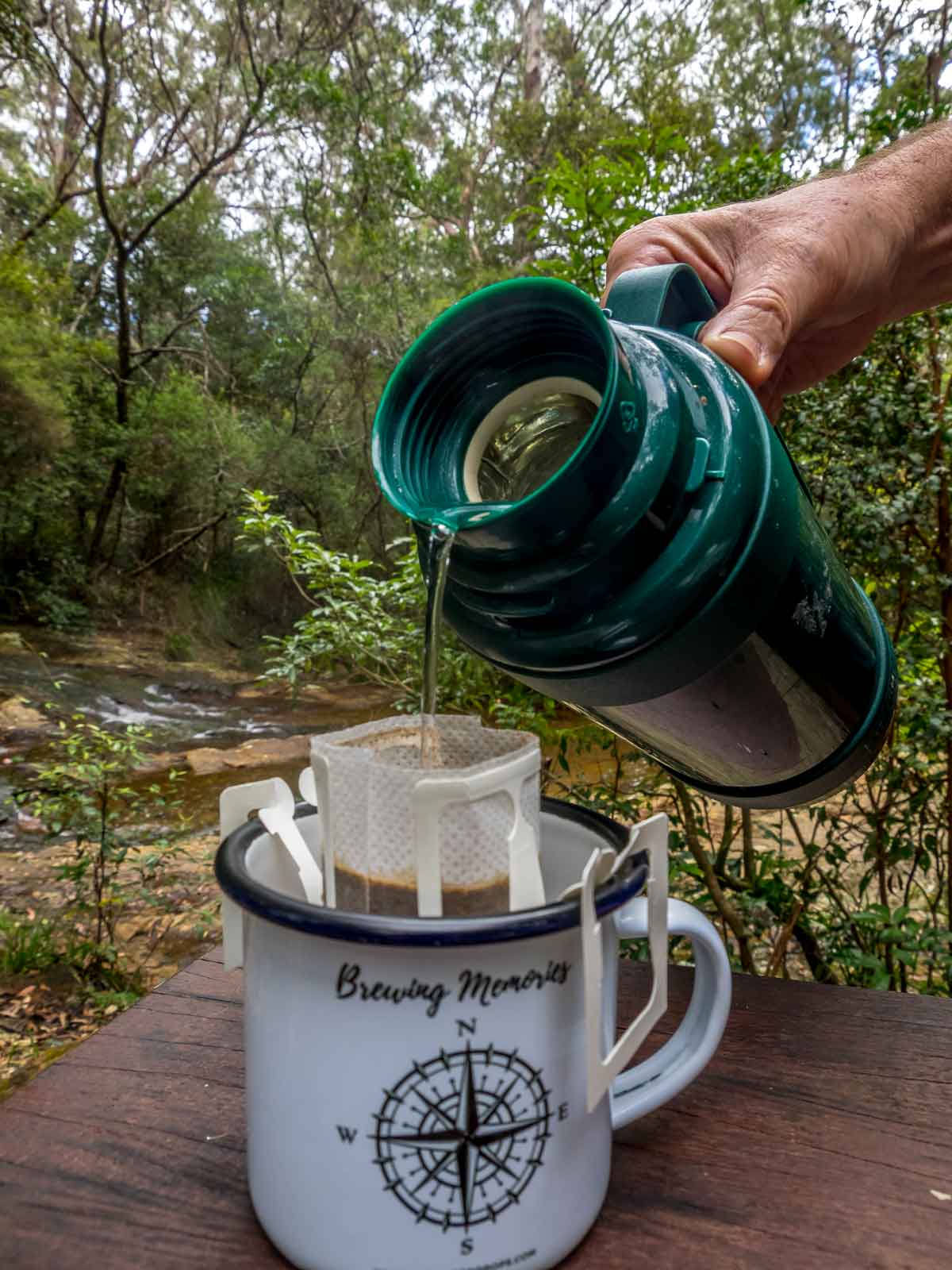 menuangkan air dari termos ke dalam cangkir dengan kantong kopi tetes di pegunungan