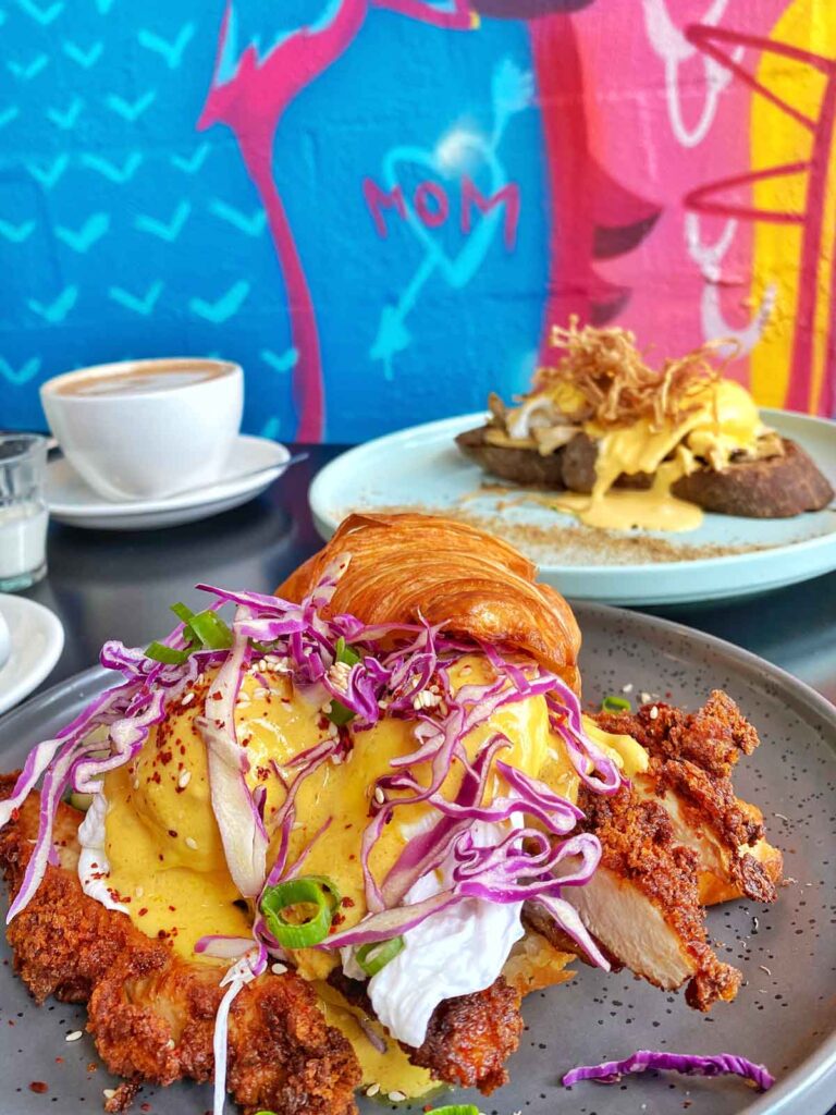 Croissant eggs benny in front of colourful cafe wall